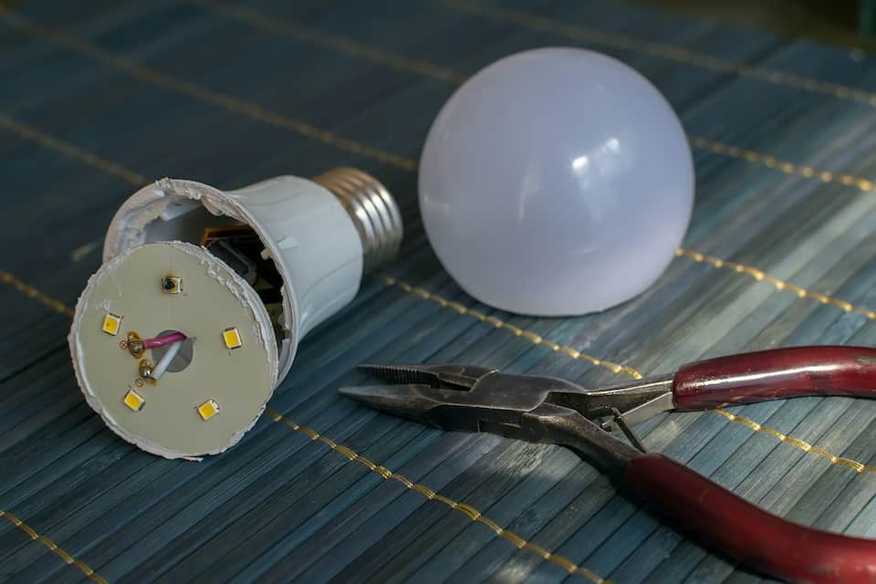 faulty, disassembled led household lamp with a burnt led element is on the table next to the pliers; how to put out an electrical fire