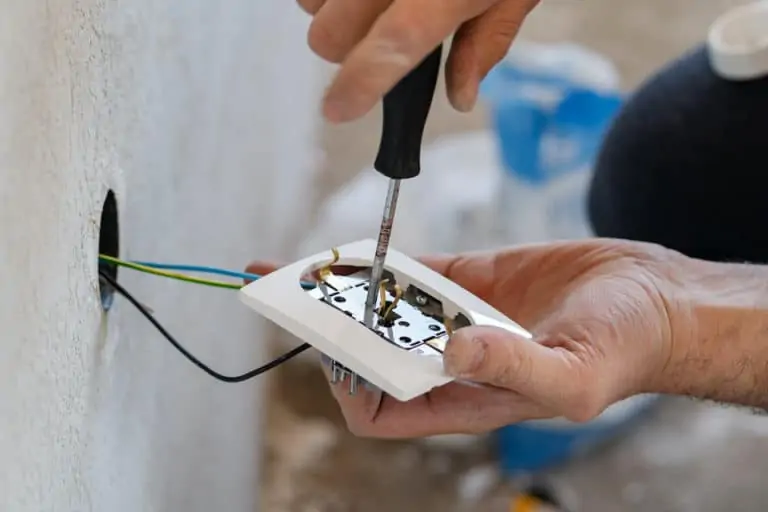 Close up on hands of caucasian man electrician holding screwdriver working on the plug electric on residential electric system installing white AC power socket on gray wall at home repair close up: outdoor outlet not working