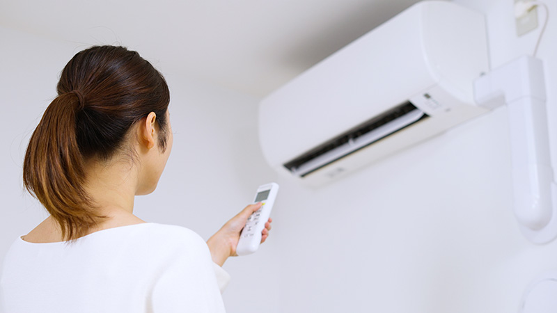 With their back turned away, a person aims a remote control at their ductless mini-split AC unit.