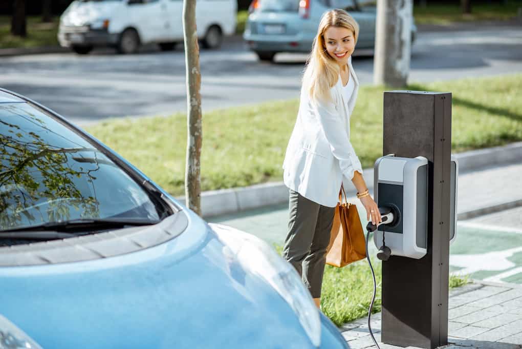 woman plugging in electric vehicle; apartments in ev charging