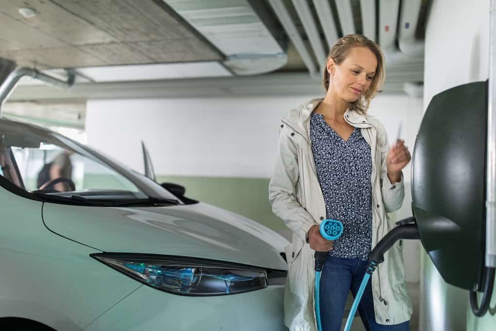 apartments with ev charging; woman plugging in ev vehicle