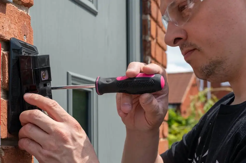 Man installing a smart doorbell with security camera and solar charger next to the front door of his house; doorbell wiring