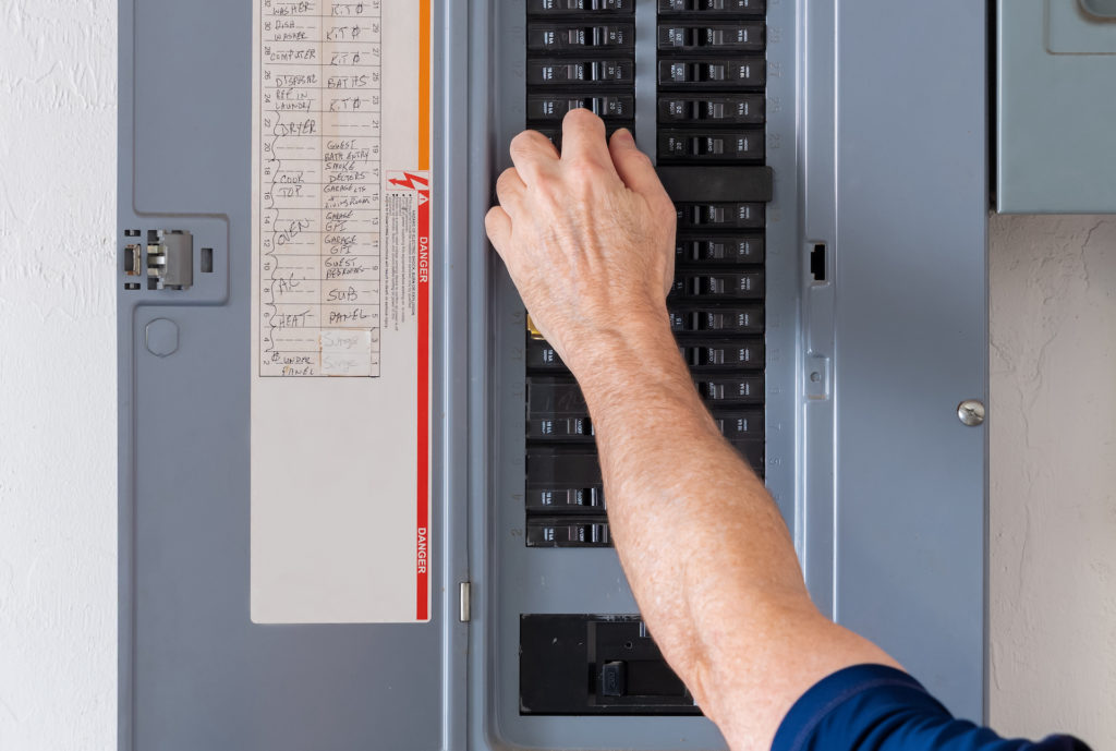 man flipping a switch off on his main electrical panel; how to install a ceiling fan