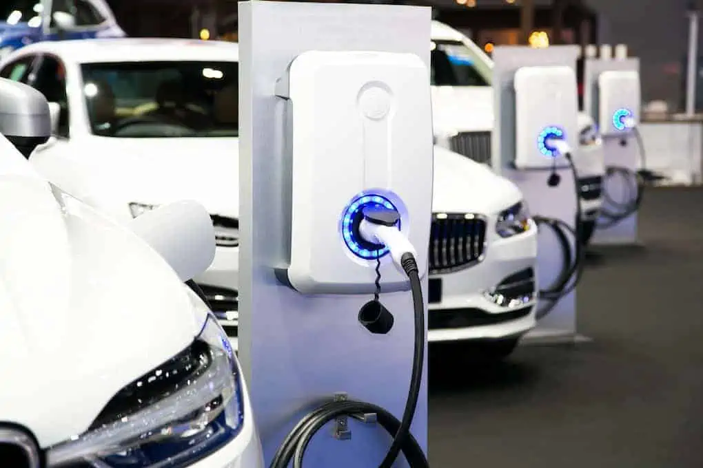 row of white electric cars plugged into charging station; how long does it take to charge an electric car