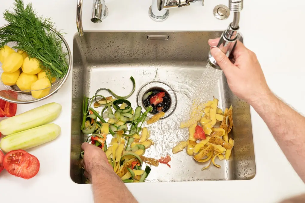 hands cleaning and peeling vegetables in sink; how to install a garbage disposal