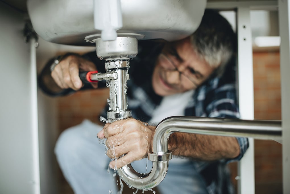 man diying emergency plumbing issue under kitchen sink without Minneapolis plumbing permit