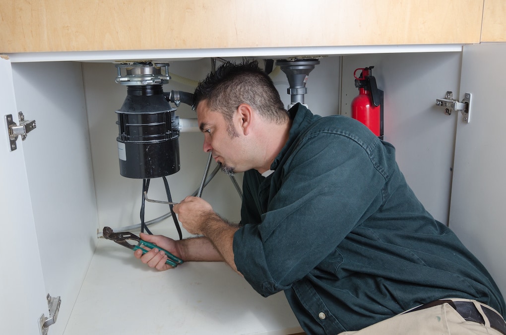 A plumber under a sink working on a garbage disposal install project that does not need a Minneapolis plumbing permit.