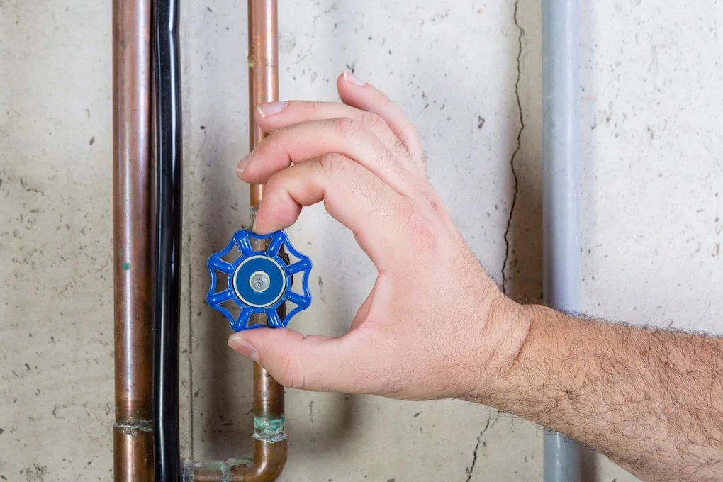 Male hand turning blue valve on copper pipe; minnesota plumbing code
