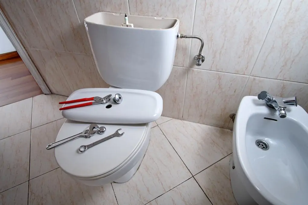 Open and damaged toilet with tools for repair and toilet water supply line pipe