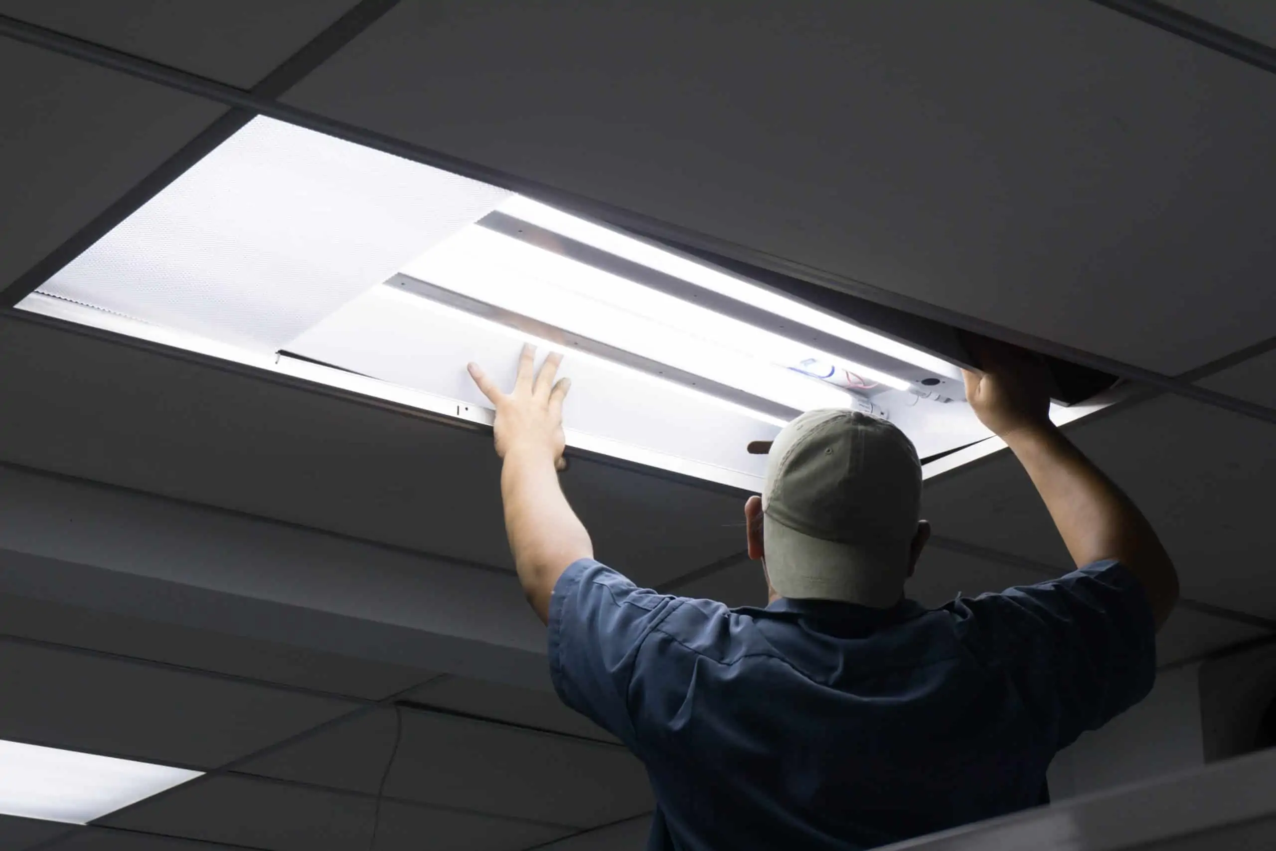 With their back turned away from the camera, an electrician removes a ceiling light panel.
