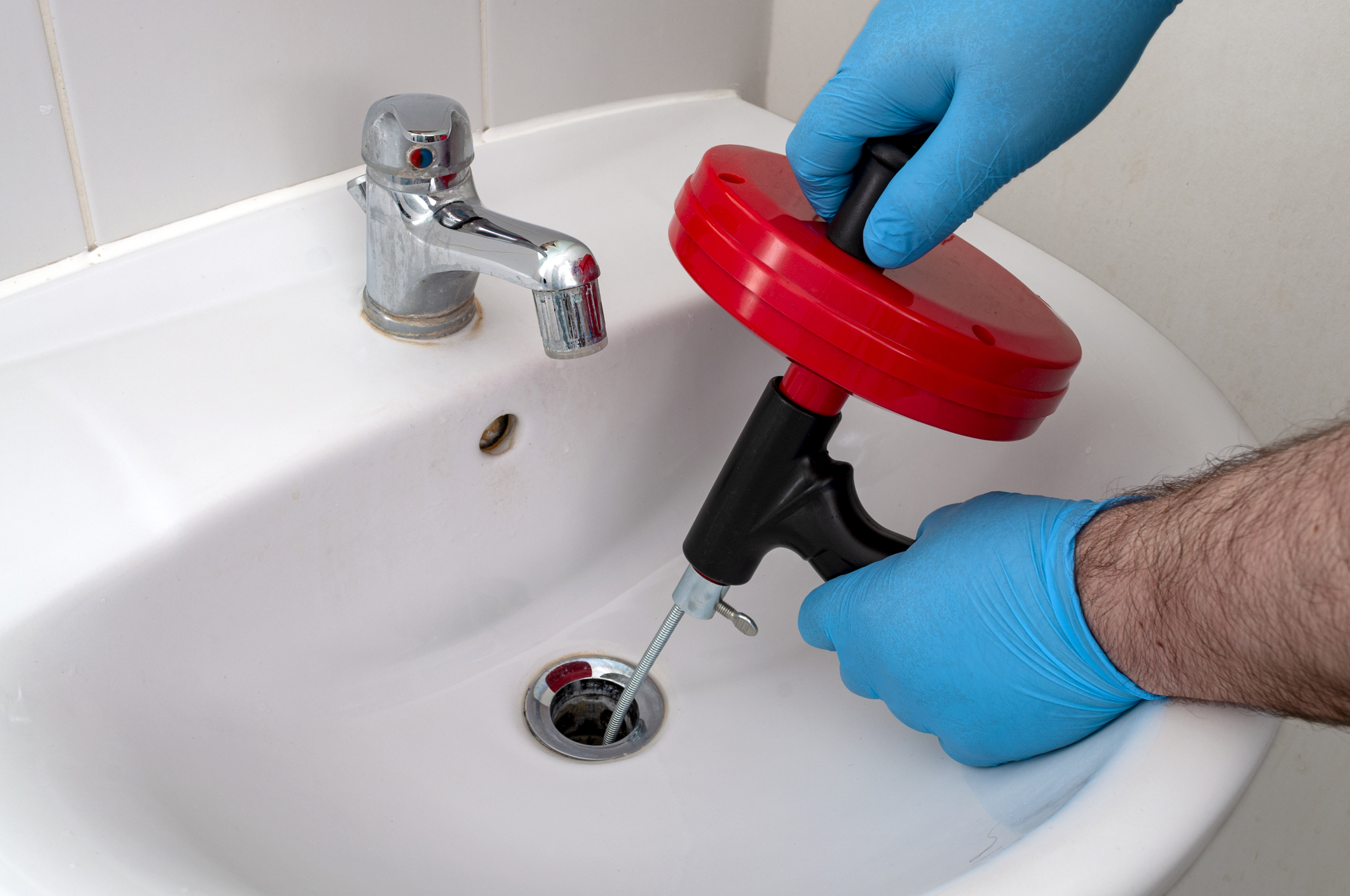 Gloved plumber snaking bathroom sink drain