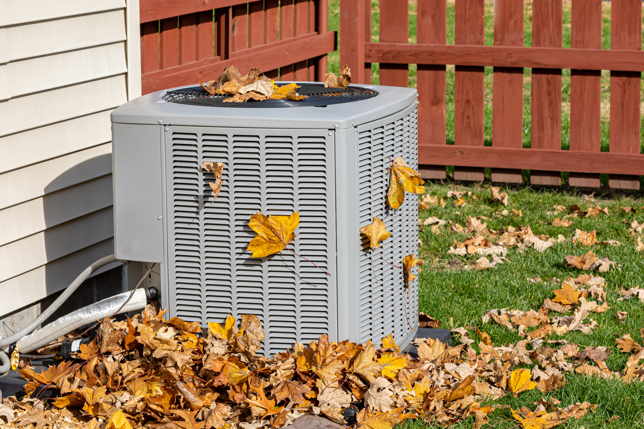 AC condenser unit in backyard of house, surrounded by leaves