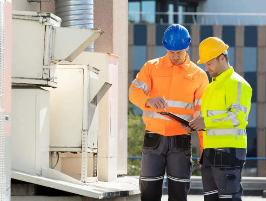 Two technicians wearing high-visibility jackets and helmets on a rooftop