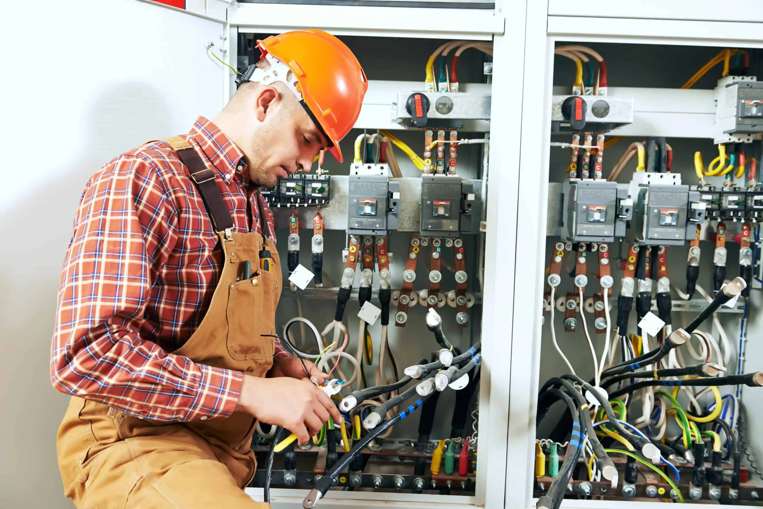 An electrician with an orange construction hat and overalls on uses a tool to bend wire.