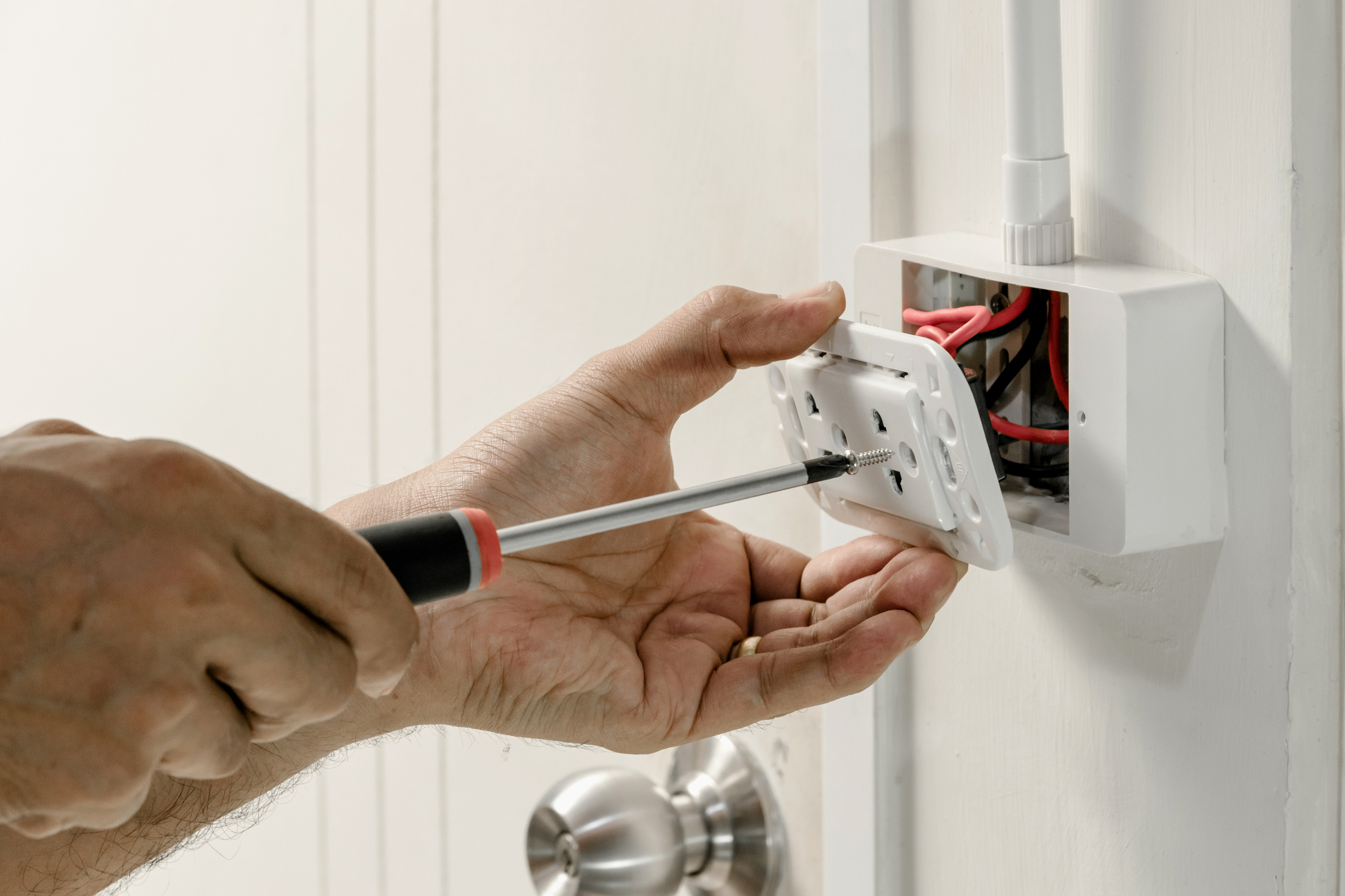 Electrician using a screwdriver to reattach an outlet cover