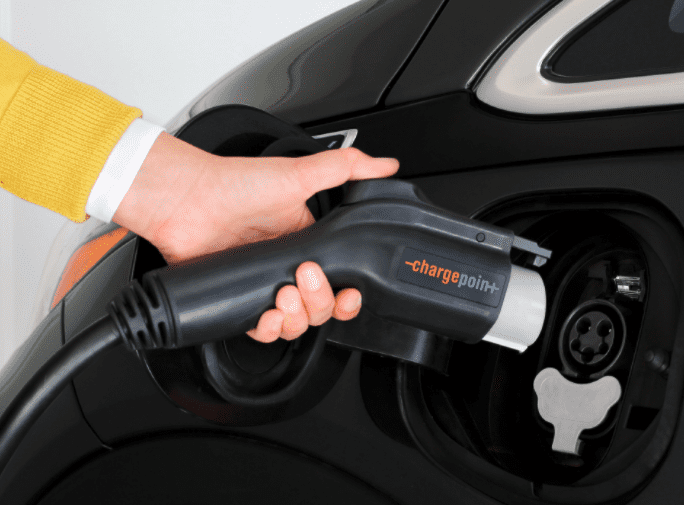 A person plugging a ChargePoint charger into their black electric car