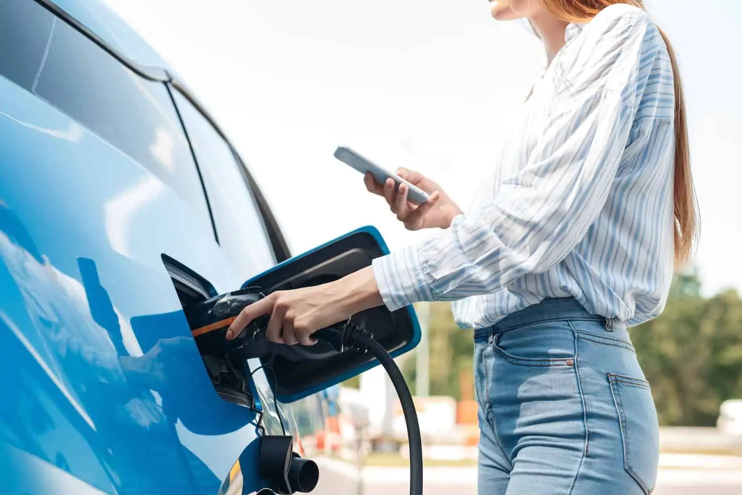 young woman charges her electric vehicle at a free public charging station