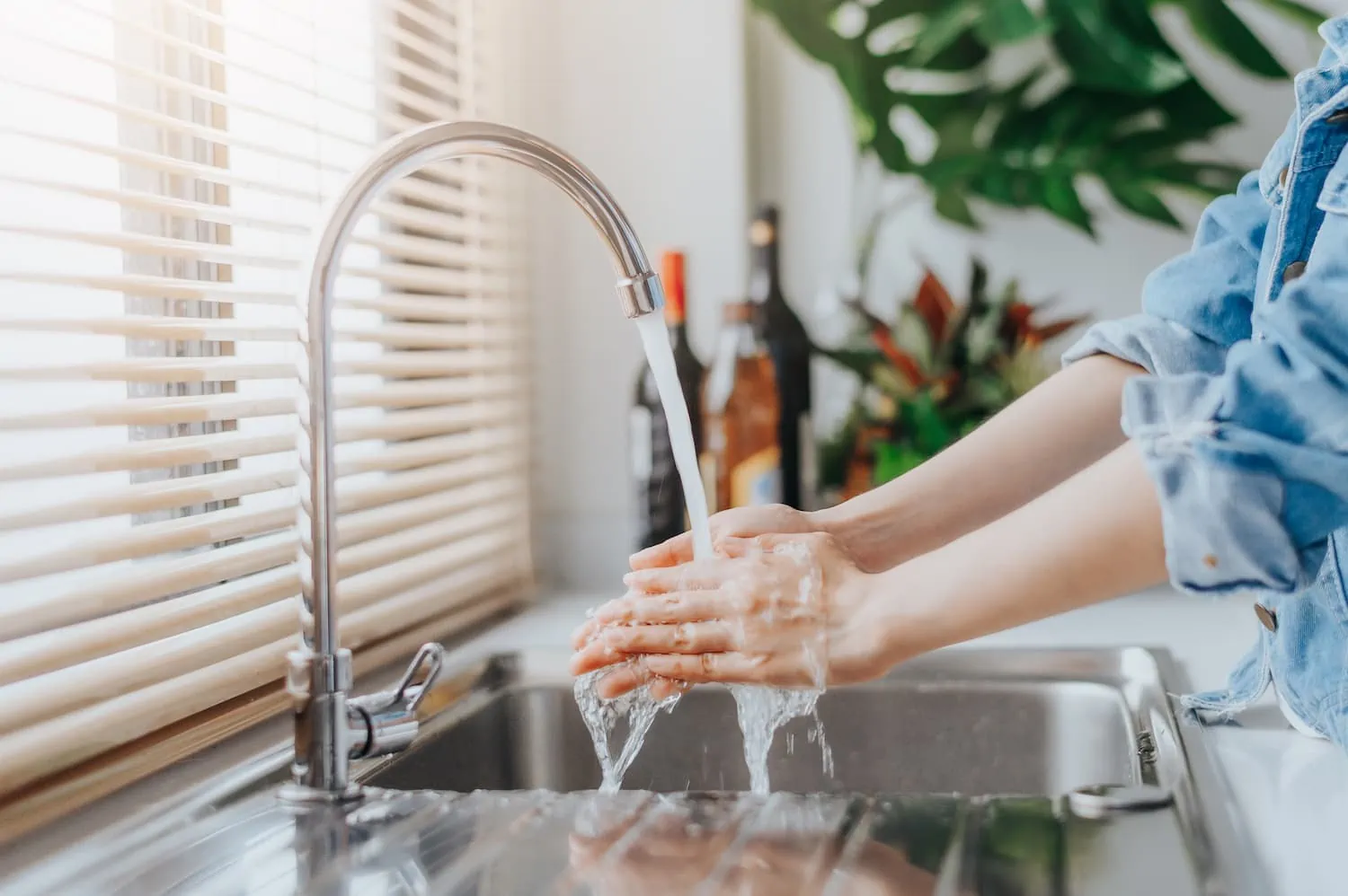 With only their hands & arms visible, a person rinses their hands under a faucet with running water.