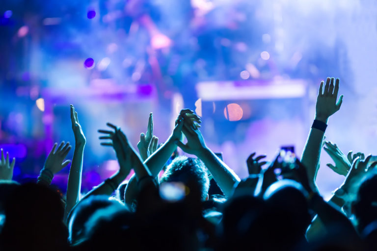 A lively concert scene with audience members raising their hands in the air