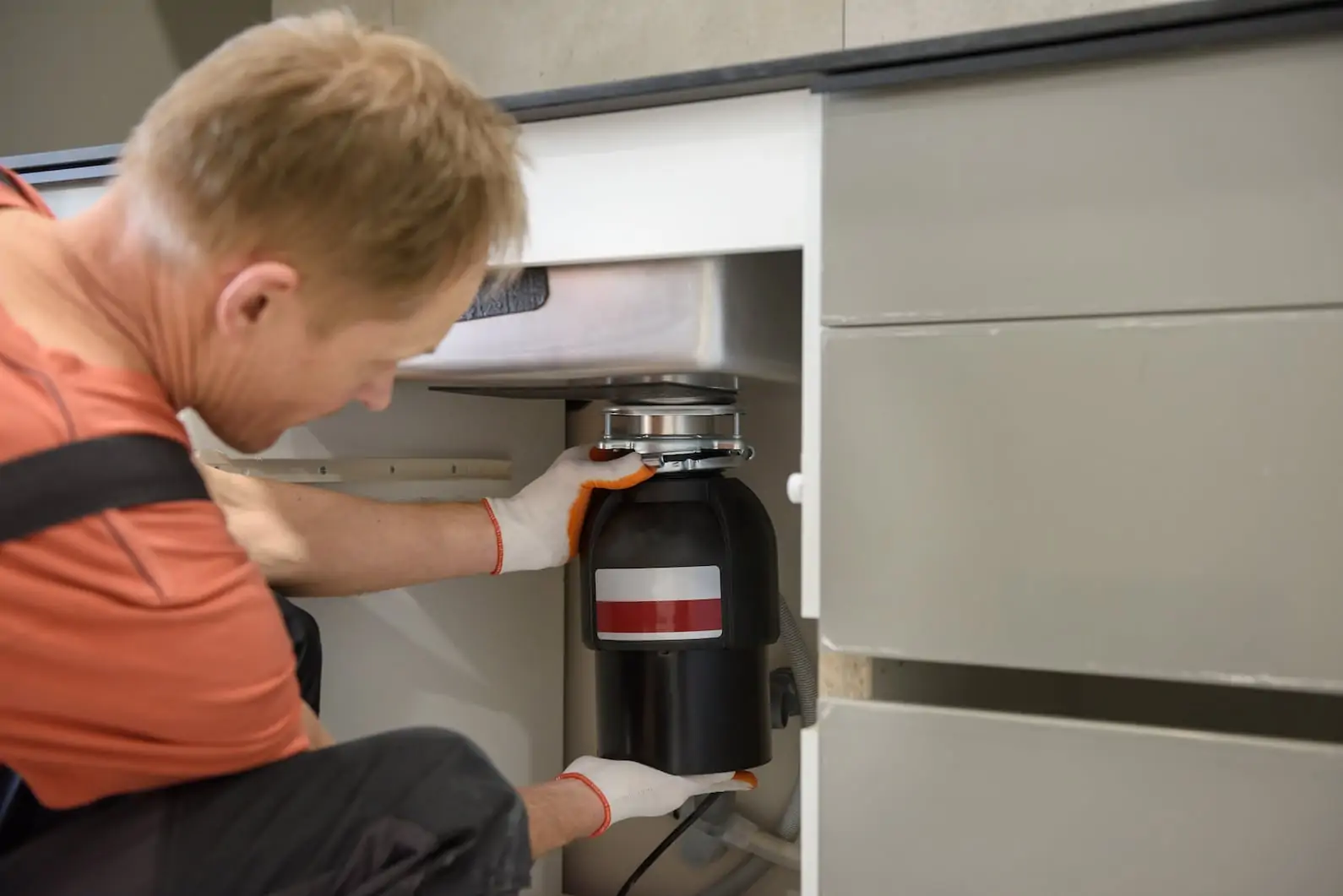 A plumber installing a disposal underneath the sink