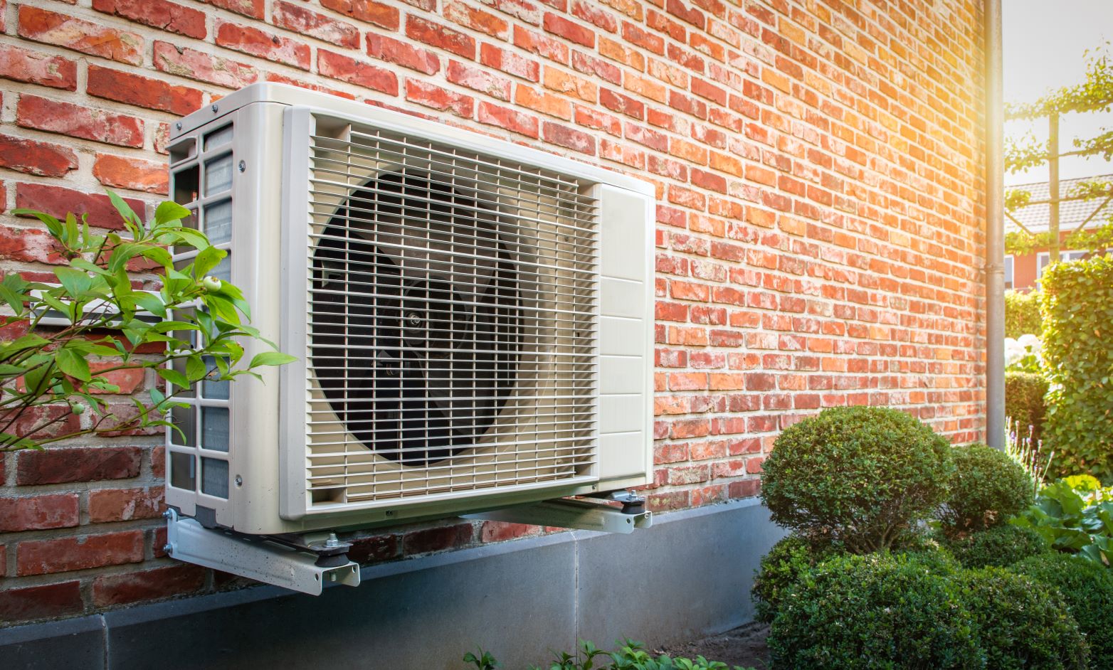 Mounted heat pump against a brick wall with sun shining on it