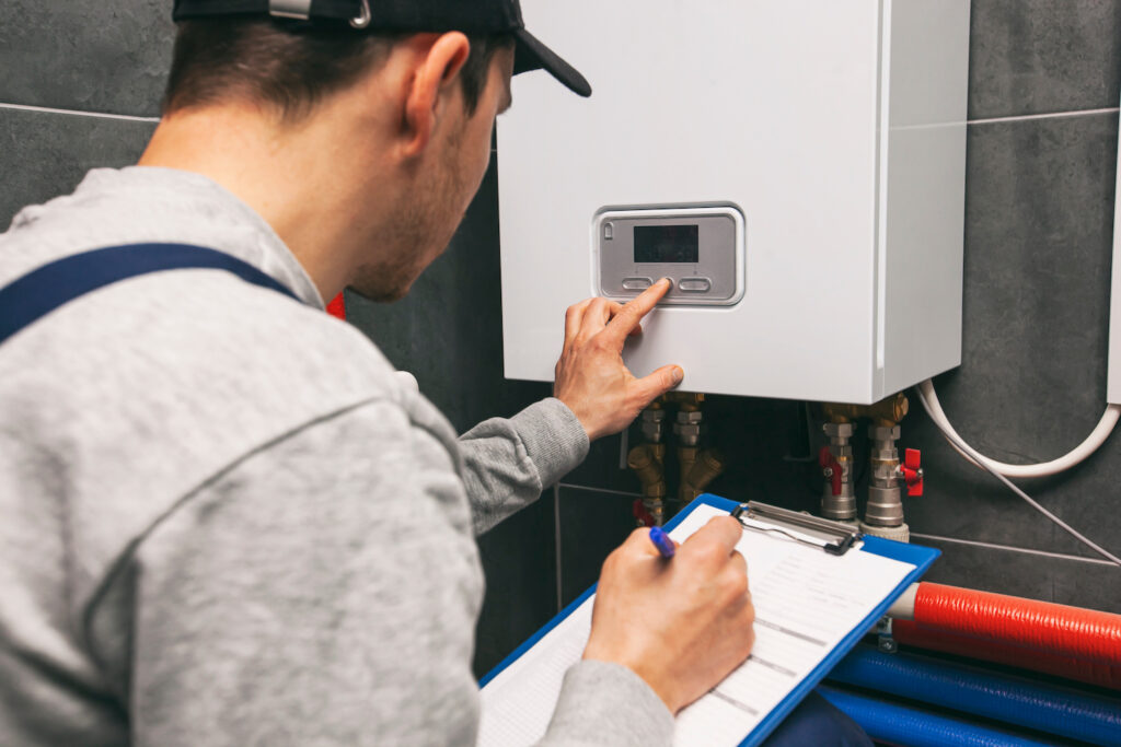 A plumber pushing a button to test a water heater & taking notes on findings.