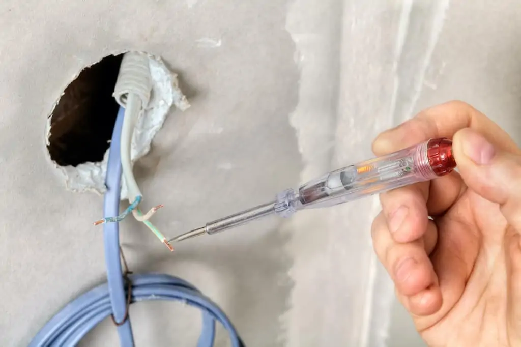 Close-up of a hand electrician check the phase of the electric wire, using an electric tester; how to install a ceiling light