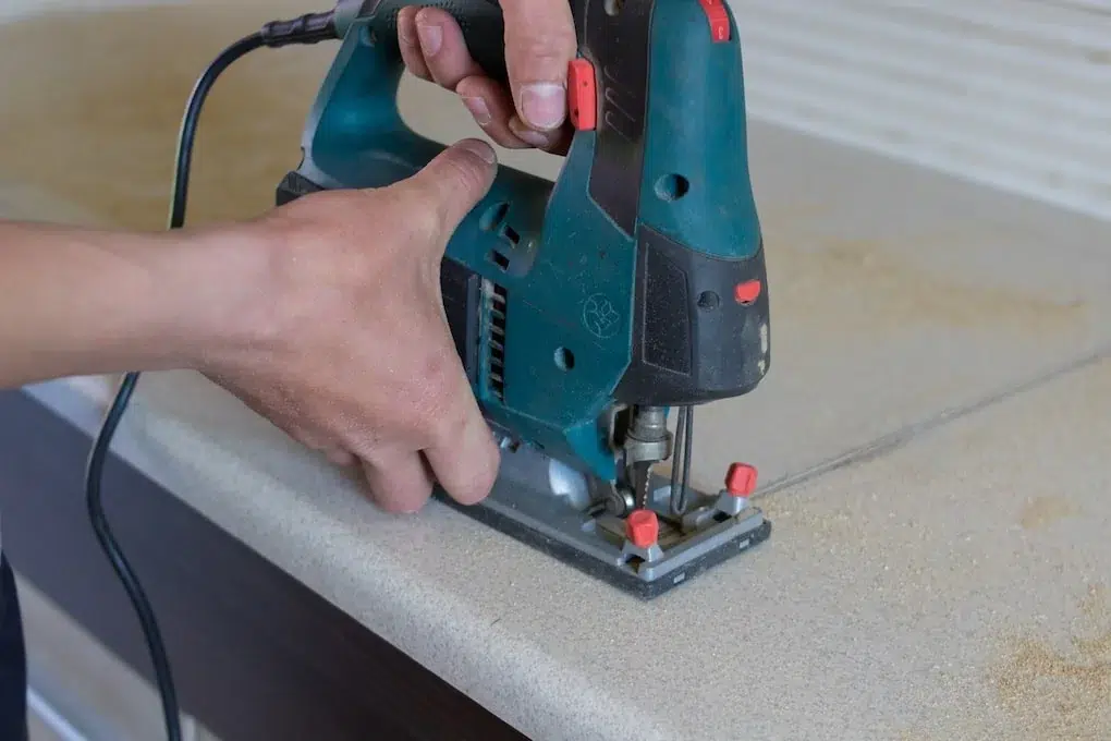 man cuts the countertop furniture on the kitchen sink electric jigsaw; hot to install a kitchen sink