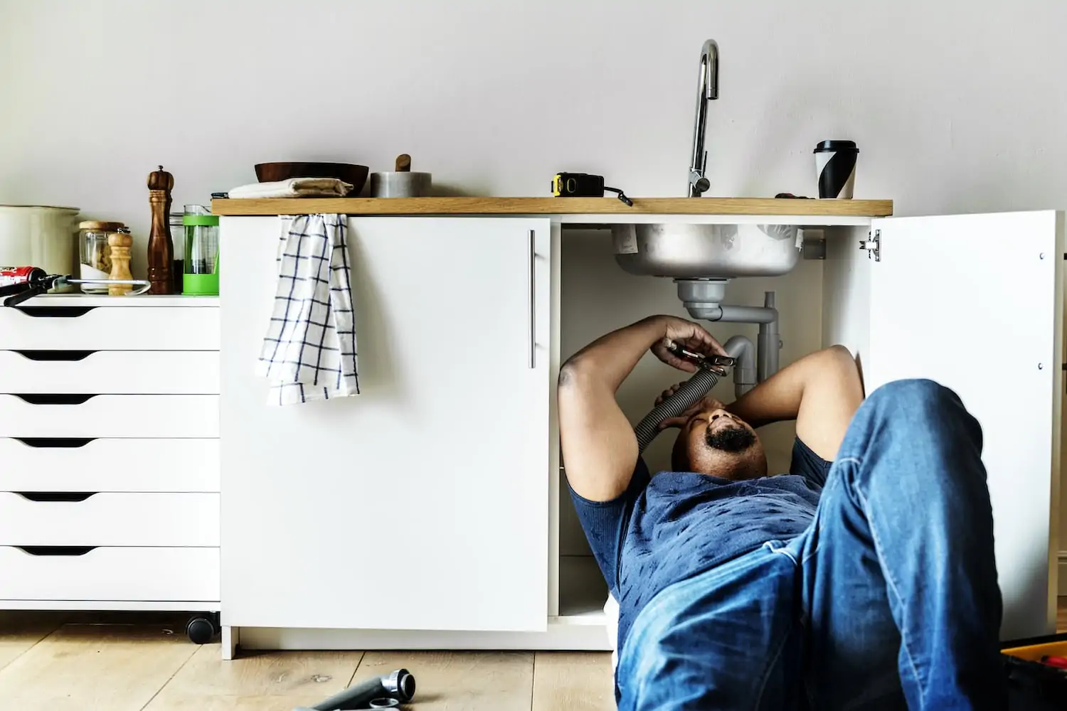 Plumber repairing a sink plumbing issue under the kitchen sink