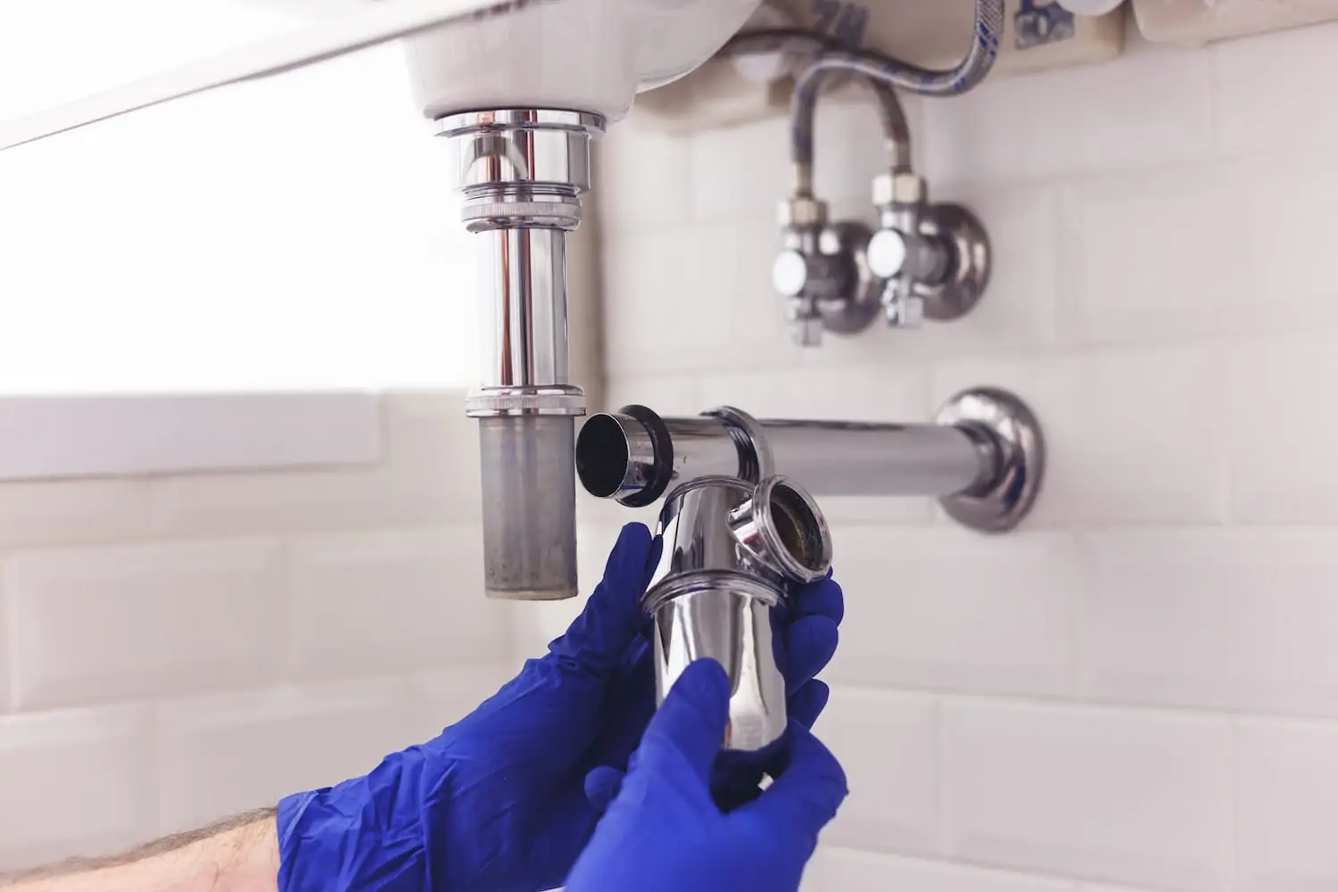 Plumber handling metal piping, showcasing a specific unattached piece under a kitchen sink