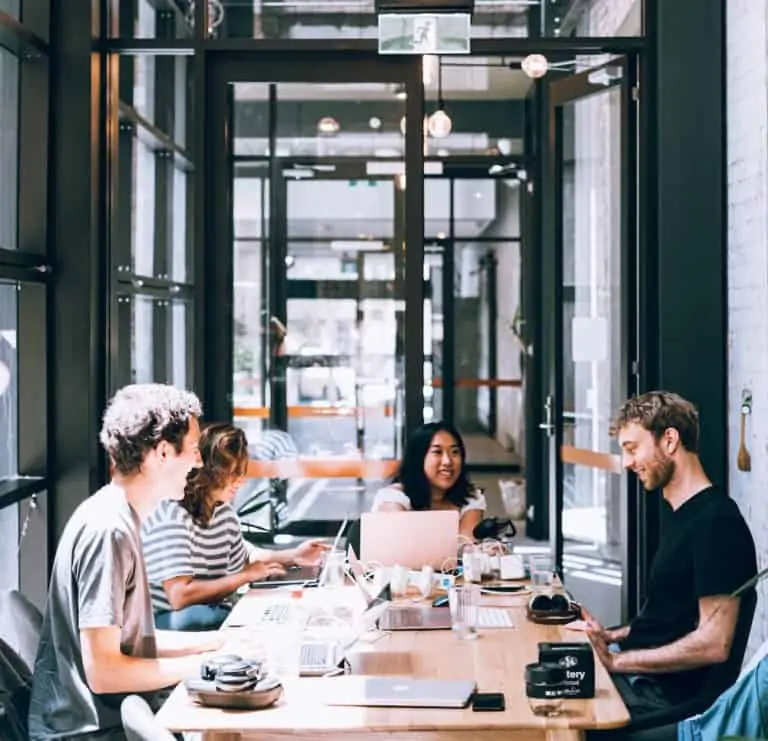 A group of people sitting around a table smiling, their laptops spread out in front of them.