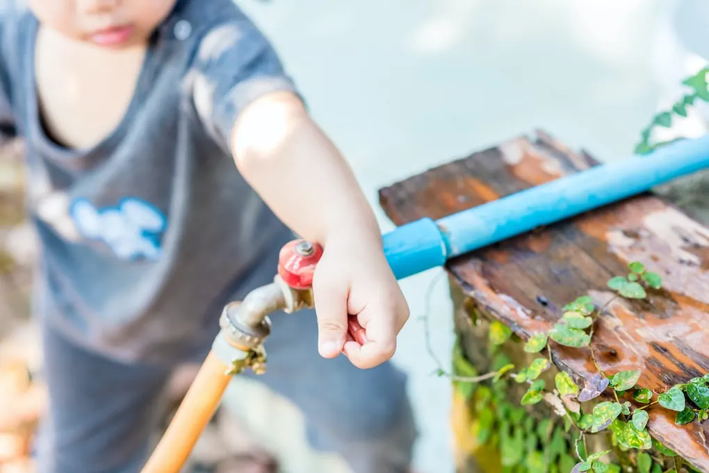 little boy turning on outdoor faucet